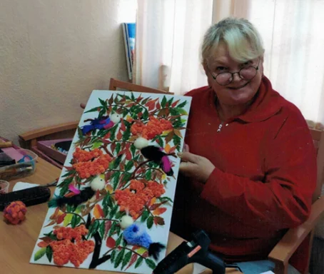 Frau mit roten Pullover hält ein farbenfrohes Kunstwerk mit Vögeln und Blumen.