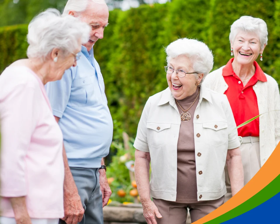 Vier ältere Personen lachen und unterhalten sich in einem Garten.